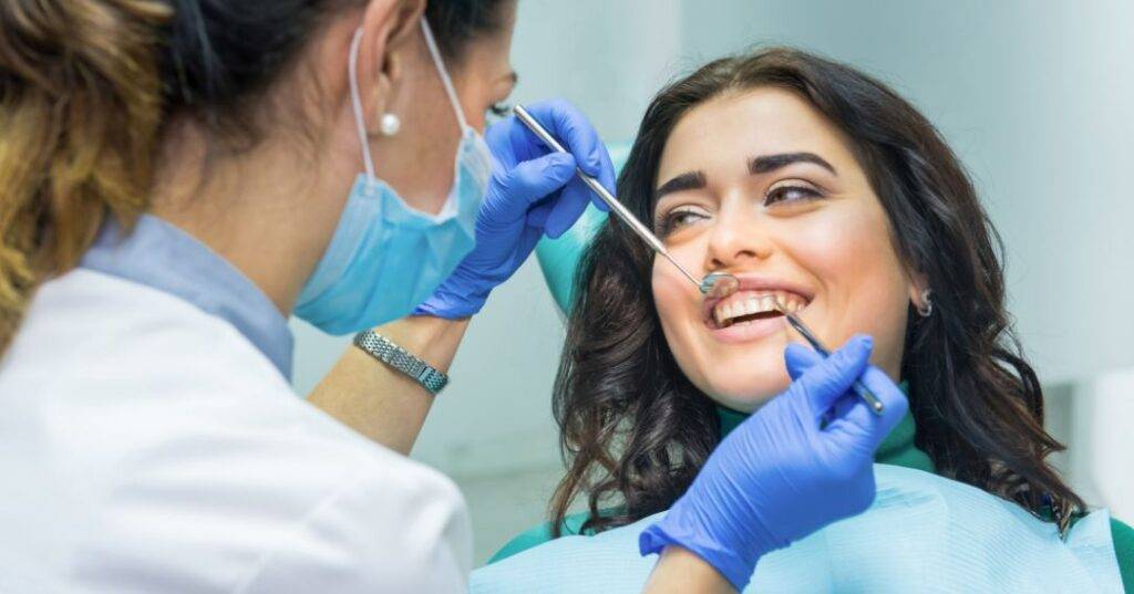 A dentist holding up tools to a patient's mouth.